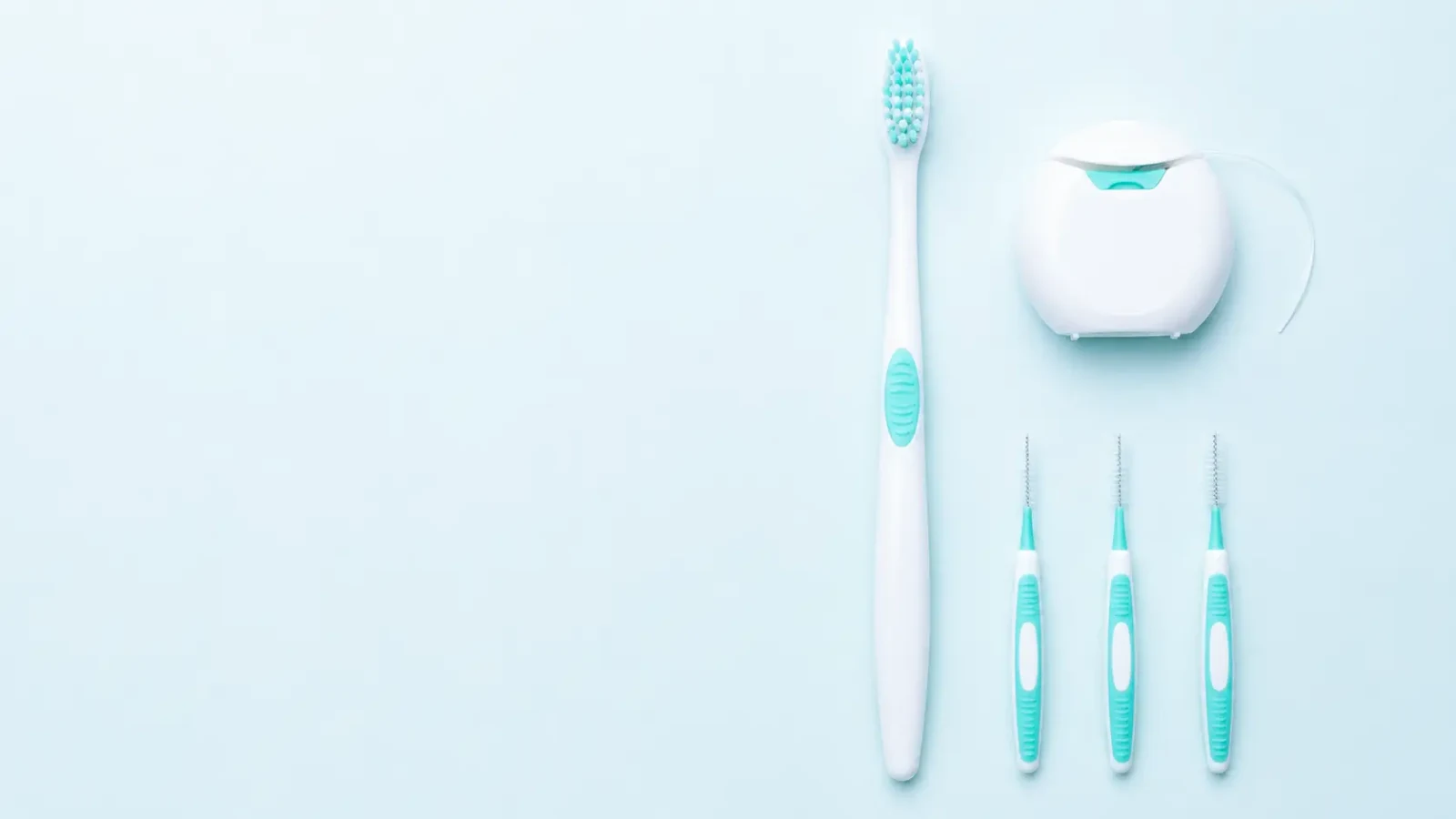 A toothbrush, dental floss dispenser and three interdental brushes arranged on a pale blue background.