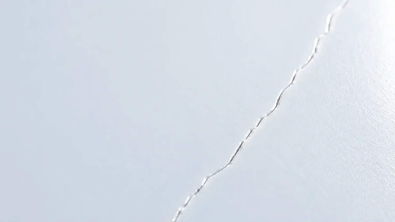 A fine hairline crack running diagonally across a smooth white surface.