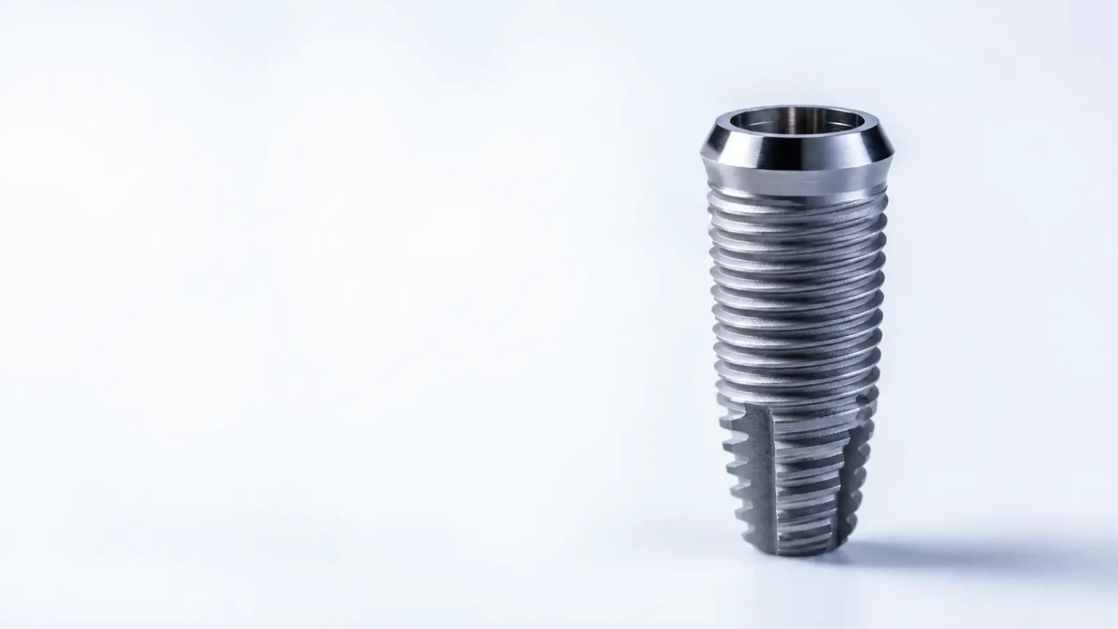 A titanium dental implant with a threaded surface standing upright on a white background.