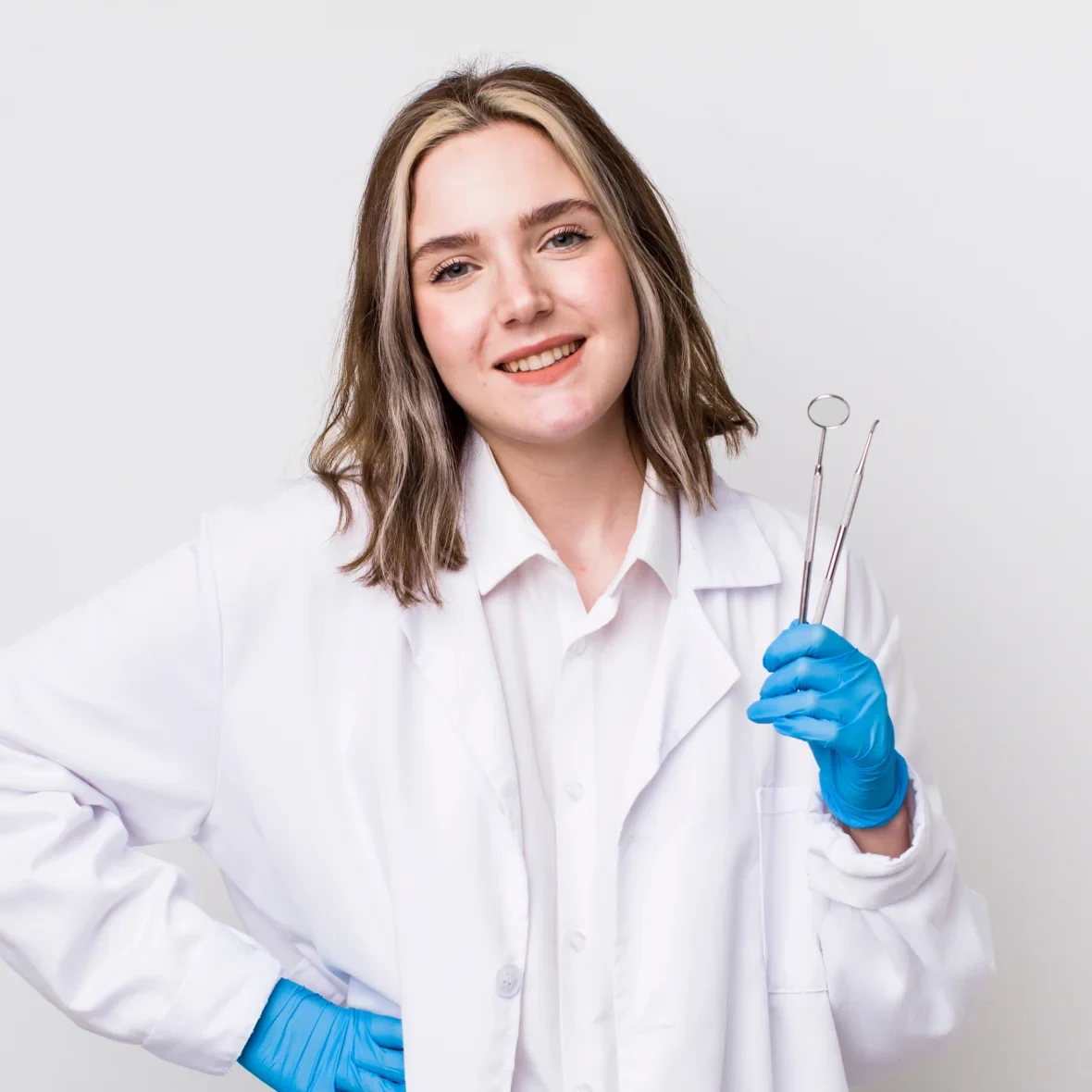 A smiling dentist wearing a white coat and blue gloves.