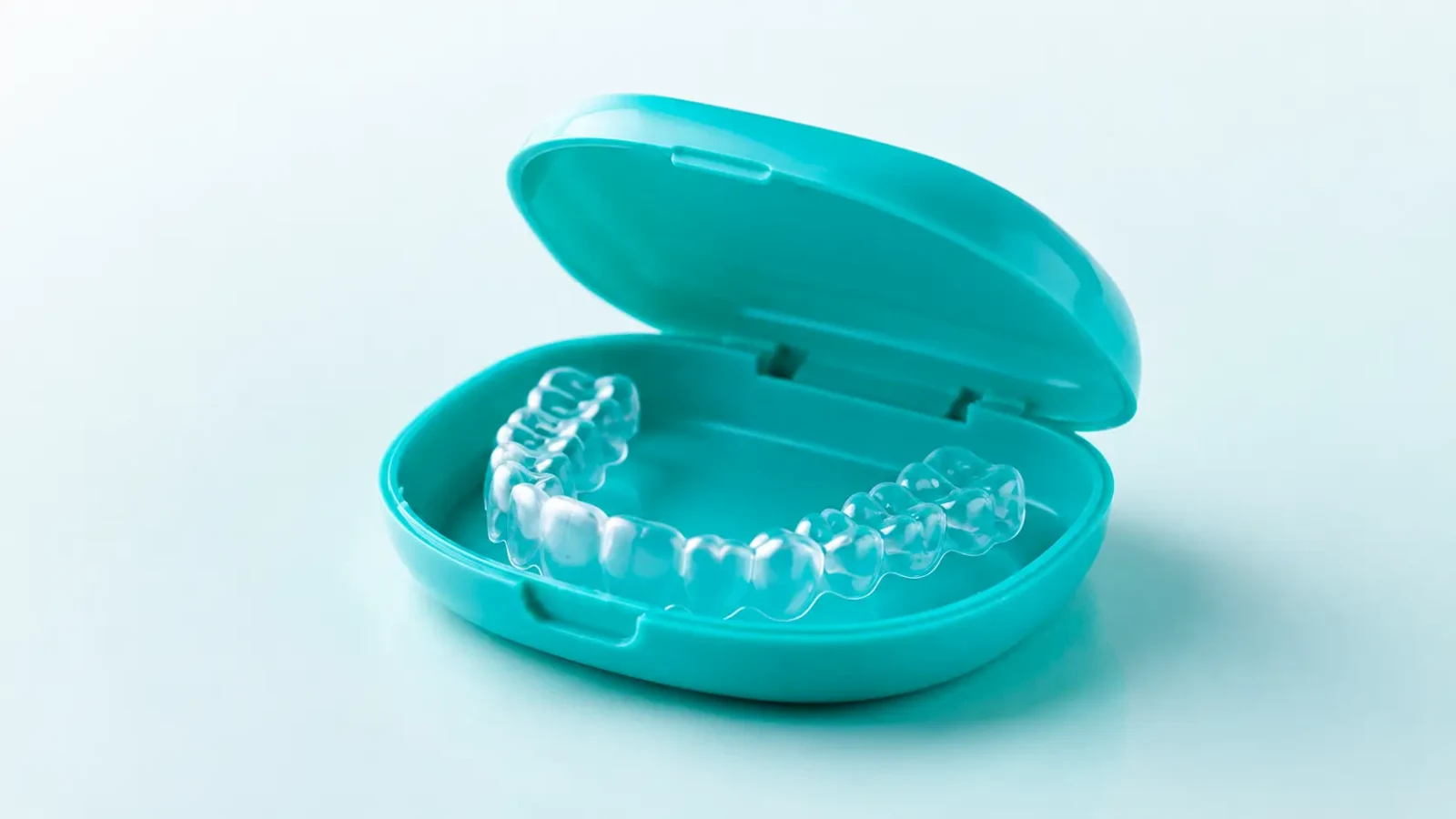 A clear dental retainer resting in an open teal storage case.