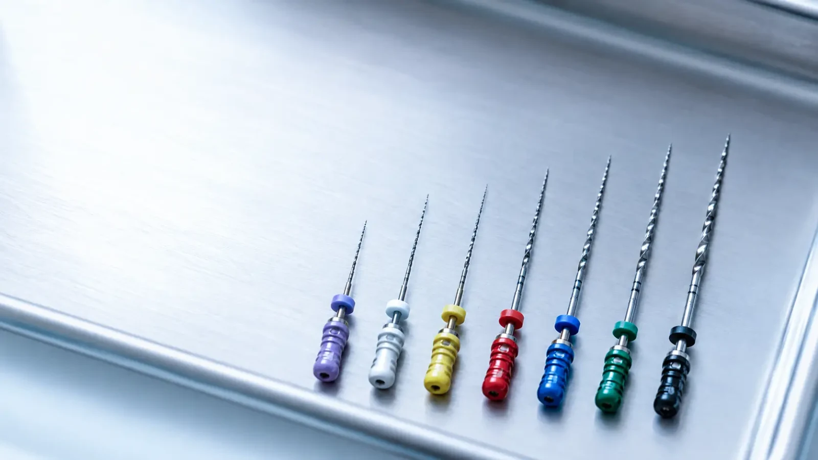 A row of colour-coded endodontic files arranged in ascending size on a stainless steel clinical tray.