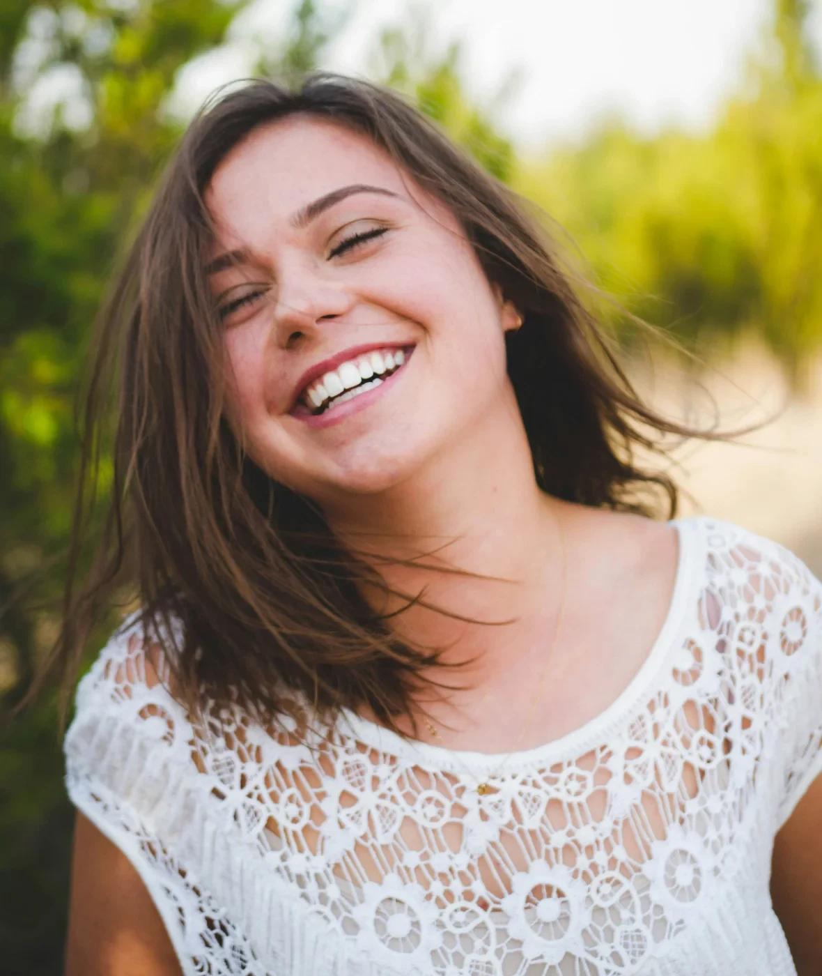 A smiling woman outdoors in soft daylight.