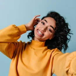A smiling woman in a yellow sweater touching her hair.